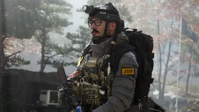 An operator with a heavy pack and helmet gear, teammates holding rifles behind him